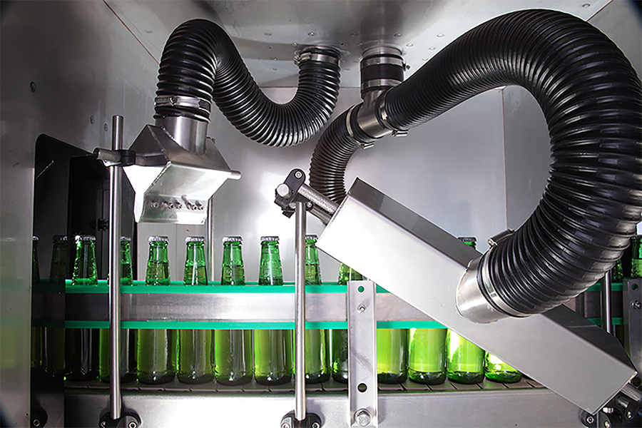 Close up of bottles on a conveyor passing through a series of air knives and hoses as part of an air drying system